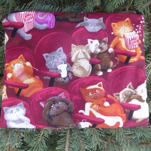 May include: A red fabric pouch with a repeating pattern of cats watching a movie in a theater. The cats are wearing different expressions and holding snacks. The text "Kitty Corn" is visible on the pouch.