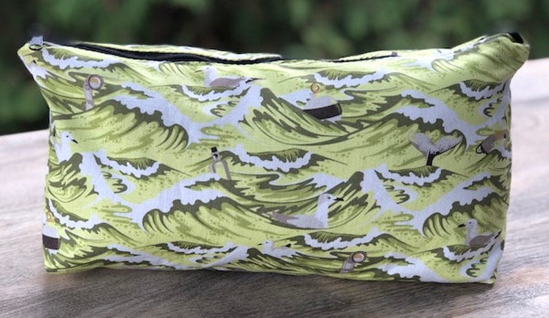 May include: A green and white zippered pouch with a repeating pattern of stylized waves and seagulls.