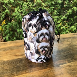 May include: A white drawstring bag with a black drawstring. The bag is covered in a pattern of Shih Tzu dog faces.