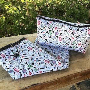 May include: Two black and white zippered pouches with a white background and a pattern of colourful Mahjong tiles. The pouches are made of fabric and have a drawstring closure.