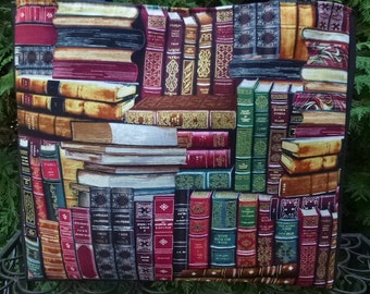 May include: A black tote bag with a colorful print of stacked books. The books have various colors, including red, green, blue, and gold. The print is a realistic depiction of a bookshelf filled with books.