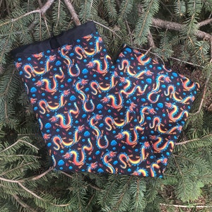 May include: Black fabric with a repeating pattern of blue, orange, and yellow dragons on a black background.