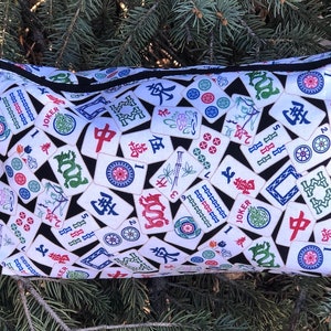 May include: A black zippered pouch with a white background and a pattern of colorful Mahjong tiles. The tiles feature Chinese characters, numbers, and symbols.