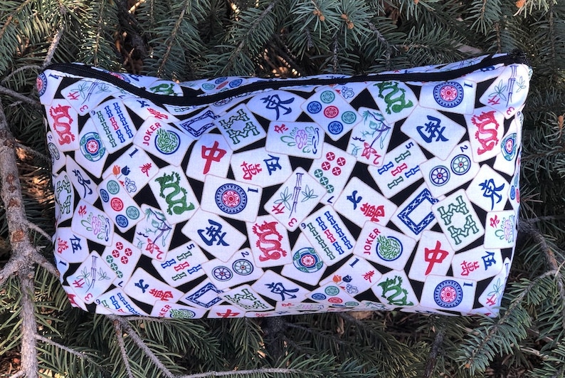 May include: A black zippered pouch with a white background and a pattern of colorful Mahjong tiles. The tiles feature Chinese characters, numbers, and symbols.