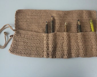 May include: A beige crocheted pencil roll with six slots for pencils. The roll is open and has a brown cord with a gold metal clasp.