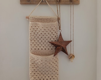 May include: A beige crocheted wall hanging with two pockets and a wooden dowel rod at the top. A copper star ornament hangs from the top of the wall hanging.