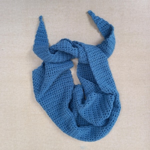 Puede incluir: Una bufanda infinita azul tejida a ganchillo. La bufanda está hecha de un hilo suave y texturizado y está diseñada en un bucle continuo. La bufanda es de color azul liso y se muestra sobre un fondo neutro. Es un accesorio versátil.