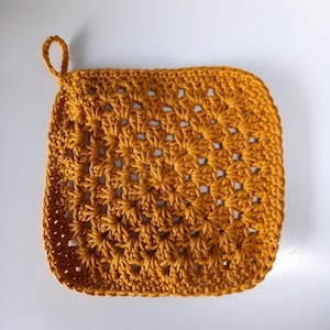 May include: Mustard yellow crocheted potholder with a loop for hanging. The square-shaped potholder features a textured, open weave design. The handmade kitchen item is a warm, inviting color.