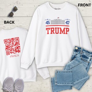 May include: White sweatshirt with the word "TRUMP" in red block letters. Above the word "TRUMP" is a graphic of the White House and the numbers "45" and "47". The back of the sweatshirt has a red QR code and the word "#MAGA".