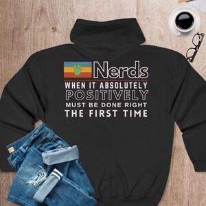 May include: Black hooded sweatshirt with a retro-style graphic that says "Nerds When It Absolutely Positively Must Be Done Right The First Time". The graphic features a green hand and a multi-colored flag.
