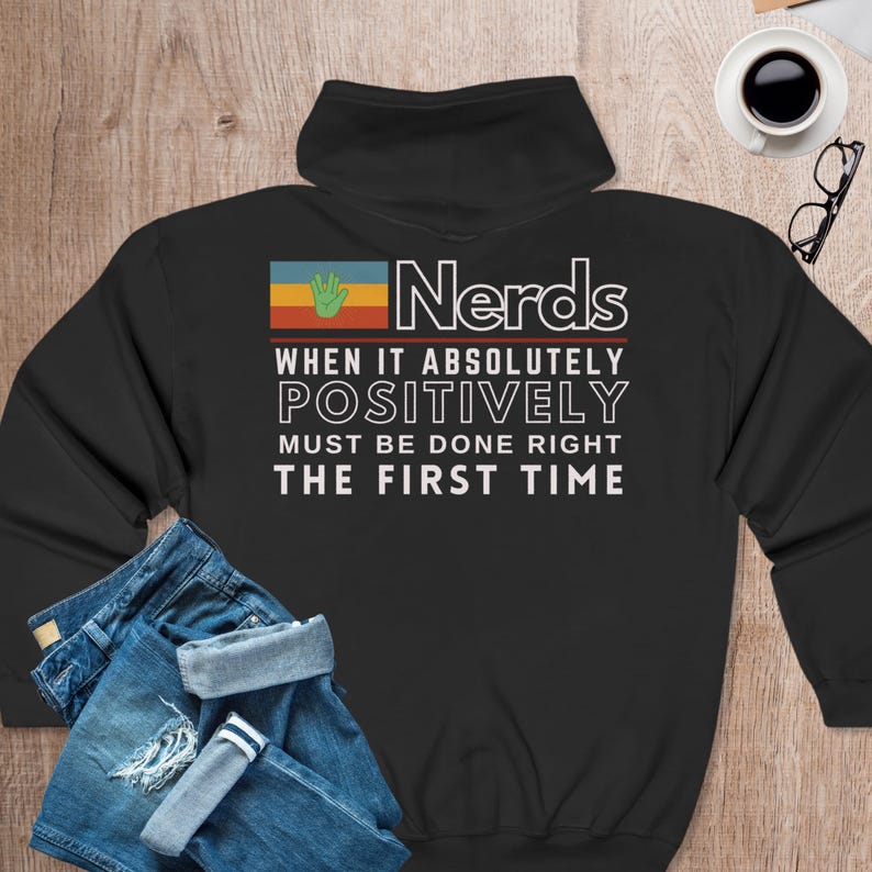 May include: Black hooded sweatshirt with a retro-style graphic that says "Nerds When It Absolutely Positively Must Be Done Right The First Time". The graphic features a green hand and a multi-colored flag.