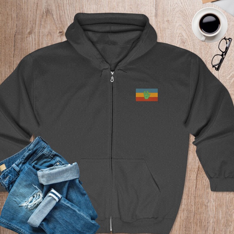 May include: A dark gray zippered hoodie with a small embroidered flag on the left chest. The flag is a horizontal tri-color of yellow, blue, and red with a green handprint in the center.