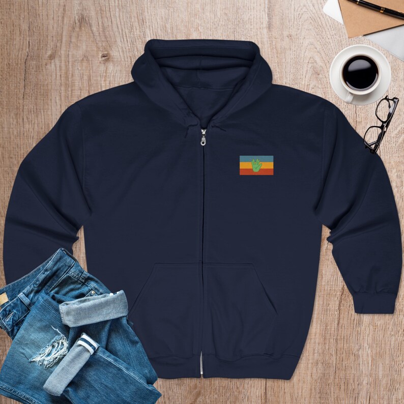 May include: A navy blue zip-up hoodie with a small embroidered flag on the left chest. The flag has a green handprint on a yellow, red, and blue background.