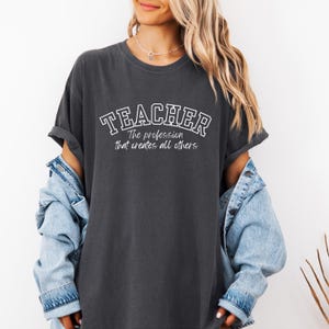 May include: A dark gray t-shirt with the text "TEACHER The profession that creates all others" in white.