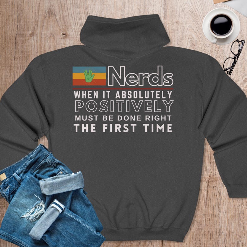 May include: Dark gray sweatshirt with a retro-style graphic that reads "Nerds When It Absolutely Positively Must Be Done Right The First Time". The graphic features a hand with a raised index finger and a colorful stripe.