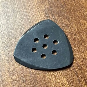 Puede incluir: Púa de guitarra negra con seis agujeros redondos. La púa está hecha de un material texturizado y tiene una forma triangular.