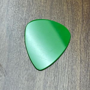 Può includere: Un plettro per chitarra verde con una forma leggermente arrotondata.
