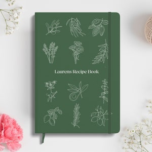 Puede incluir: Un libro de recetas verde con un contorno blanco de varias hierbas y especias en la portada. El título "Laurens Recipe Book" está impreso en blanco en la parte delantera.