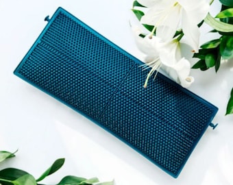 May include: A teal blue rectangular brush with a textured surface. The brush has a small handle on each end.