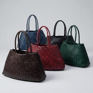 Puede incluir: Una colección de bolsos tote tejidos en varios colores. Los bolsos presentan un diseño trenzado y asas resistentes. Los colores incluyen marrón, rojo, negro, verde y azul. Los bolsos se muestran sobre un fondo neutro.