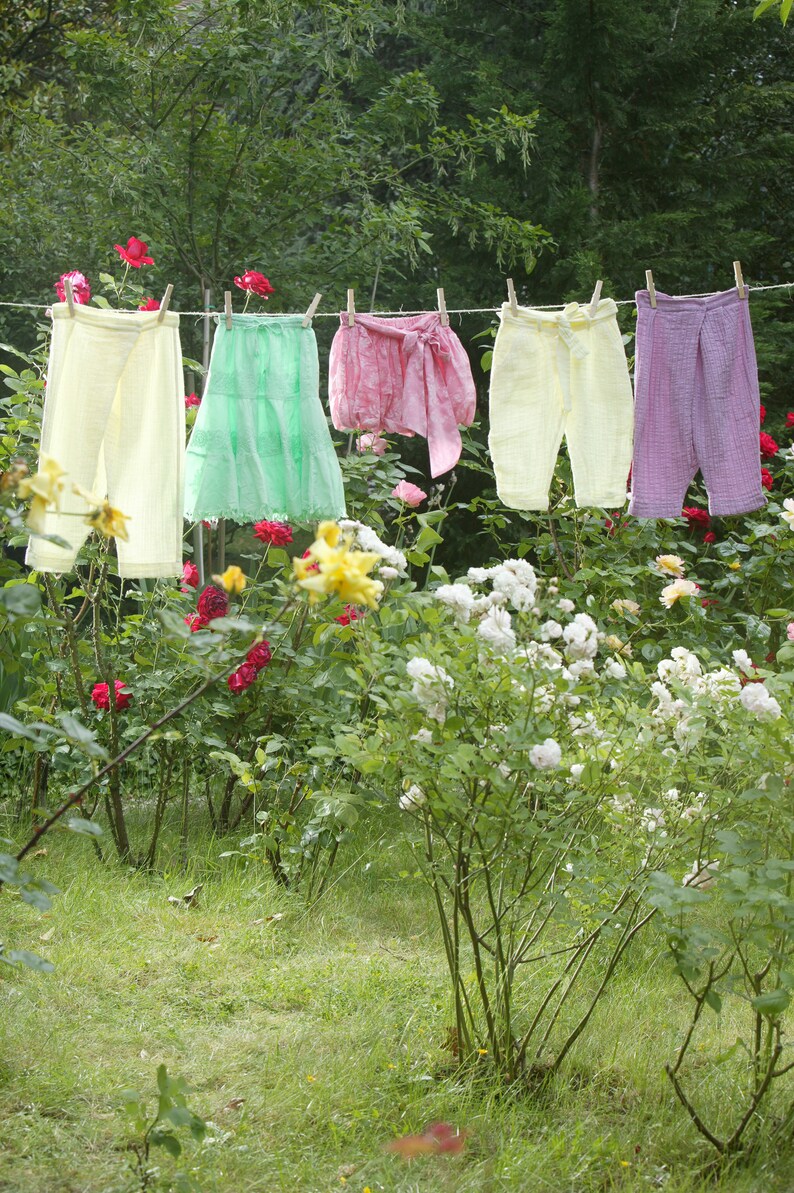 Sur un fil à étendre, dans un jardin fleuri, cinq petits vêtements colorés pour fille.