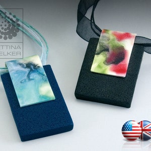 May include: Two rectangular pendants with abstract watercolor designs on a white background. The pendant on the left has a blue, green, and white design. The pendant on the right has a red, green, and black design. Both pendants are attached to black and white ribbons.