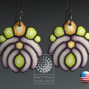 Puede incluir: Un par de pendientes de color morado, verde y naranja con un diseño geométrico. Los pendientes están hechos de arcilla polimérica y tienen una superficie texturizada.