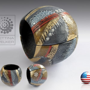 May include: A ceramic sphere with a geometric pattern in shades of grey, gold, and red. The sphere is split into two halves, revealing the intricate design.