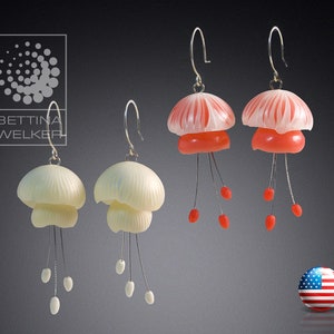 Pode incluir: Par de brincos com delicados pingentes em forma de flor com contas penduradas. Um par é branco com acabamento perolado, o outro é vermelho com um centro branco.