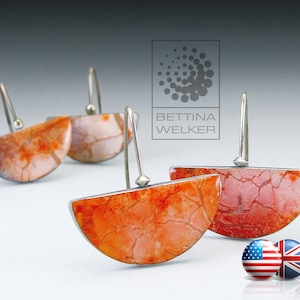 May include: A pair of silver earrings with orange and white semi-circular ceramic pieces. The ceramic pieces have a crackled finish and are set in silver.