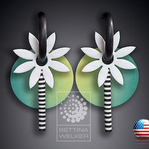 May include: A pair of black and white striped earrings with a white flower and green and yellow circle design. The earrings are made of polymer clay.