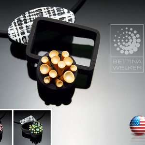 Puede incluir: Un collar negro con un colgante de patrón geométrico. El colgante está hecho de cerámica con patrón blanco y negro y tiene un grupo de pequeños círculos dorados en el centro. El collar se muestra sobre un fondo negro con el texto "BETTINA WELKER" y un logotipo de un círculo con círculos más pequeños a su alrededor.