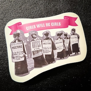 Könnte beinhalten: Aufkleber mit einem Vintage-Bild von Frauen, die Schilder mit der Aufschrift "Votes for Women Meeting" halten. Ein rosa Banner oben zeigt den Text "Girls Will Be Girls".