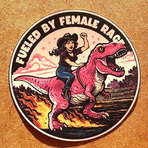 Puede incluir: Adhesivo redondo con el texto "Fueled by Female Rage". La imagen central muestra a una mujer montada en un dinosaurio rosa, con el puño en alto. Las llamas y una puesta de sol están en el fondo.
