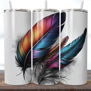 May include: White insulated tumbler featuring a vibrant design of colorful feathers. The feathers display shades of orange, purple, blue, and pink, with a black and gray smoky background. The tumbler includes a silver straw and lid.
