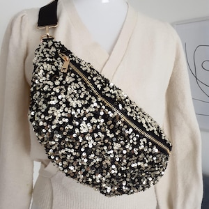 Peut inclure: Une banane noire et dorée à paillettes avec une fermeture éclair dorée. La banane est portée sur un mannequin.