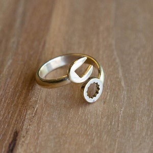 May include: A gold-toned ring shaped like a wrench with a star-shaped cutout. The ring is on a wooden surface.