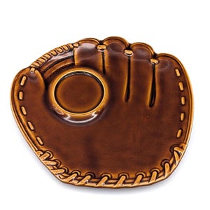 May include: A brown ceramic dish shaped like a baseball glove. The glossy, glazed surface features molded details including stitched lacing along the edges and a circular indentation in the center that mimics the pocket of a leather mitt.