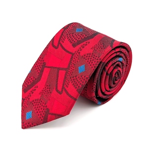May include: Rolled red necktie with a geometric pattern. The tie features a repeating design of red shapes, dark red dots, and small blue squares. The tie is made of a textured fabric.