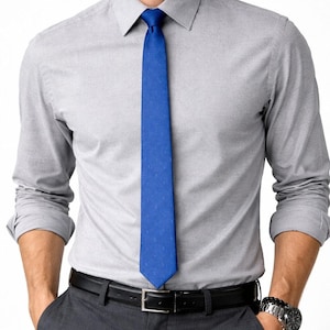 May include: A light gray long-sleeve dress shirt paired with charcoal gray trousers and a black belt. A bright blue tie is knotted at the collar. A silver watch is visible on the wrist.