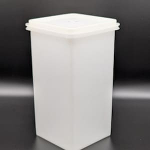 May include: A white, rectangular storage container with a matching lid. The container has a tall, slender shape and is made of opaque plastic. The lid fits snugly on top, creating a sealed compartment. The container is designed for storing various items.