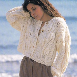 May include: A white knitted cardigan with a cable knit pattern and button closure. The cardigan is cropped and has long sleeves.