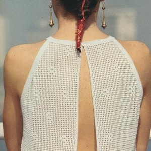 May include: A white crochet halter top with a low back and a delicate openwork pattern. The top is sleeveless and has a relaxed fit.