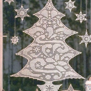 Puede incluir: Una decoración de árbol de Navidad de crochet blanco con un diseño de encaje. El árbol está colgado en una ventana con otras estrellas de nieve de crochet.