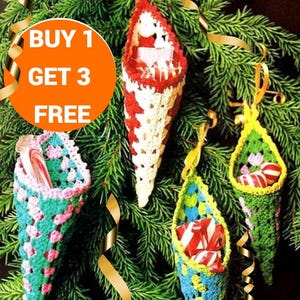 May include: Four crocheted Christmas stocking ornaments hanging on a green pine tree. The ornaments are filled with candy canes and are in red, white, green, and blue colours. The text "BUY 1 GET 3 FREE" is in a bright orange circle.