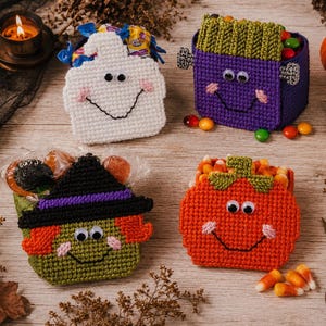 May include: Four crocheted Halloween treat baskets featuring a white ghost, a purple monster with green hair, a green witch with a black hat, and an orange pumpkin. Each basket has googly eyes, stitched smiles, and is filled with assorted candies.