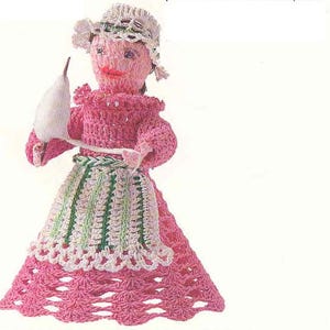 May include: A crocheted doll wearing a pink dress with a white lace trim, a white crocheted hat, and holding a white cotton ball.