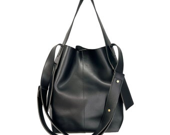 May include: A black leather tote bag with a long strap and a gold buckle. The bag has a slouchy, casual look.