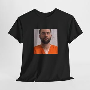Puede incluir: Una camiseta negra con una foto de un hombre con un mono naranja.