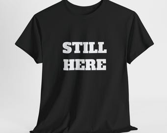 Puede incluir: Camiseta negra con texto blanco en negrita que dice "STILL HERE".